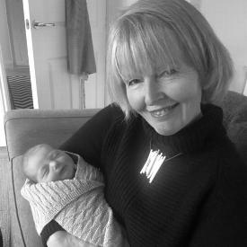 Independent Midwife Ninette Hume sits smiling holding a newborn baby