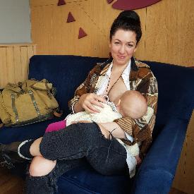 Lucy buddington independent midwife sits smiling while she holds a baby and breastfeeds