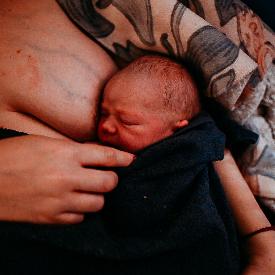 a newly born baby lays in its mothers arm, covered with a blanket