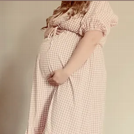 pregnant woman stands holding her tummy wearing a pink dress